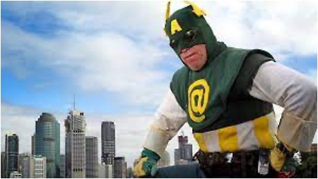 Captain Australia wears his green and gold hero uniform and takes a dynamic pose with a city skyline in the background.