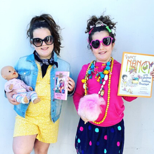 Two young girls are dressed up with beaded necklaces, sunglasses and bright clothes, they are holding prized toys and books.