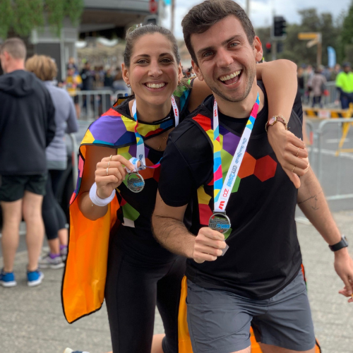 A man and a woman wearing TKCP tee-shirts celebrate arm-in-arm after winning medals in a fundraising marathon event.