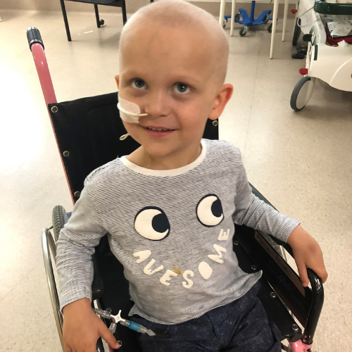 Ollie in a wheelchair at the hospital wearing a shirt that says 