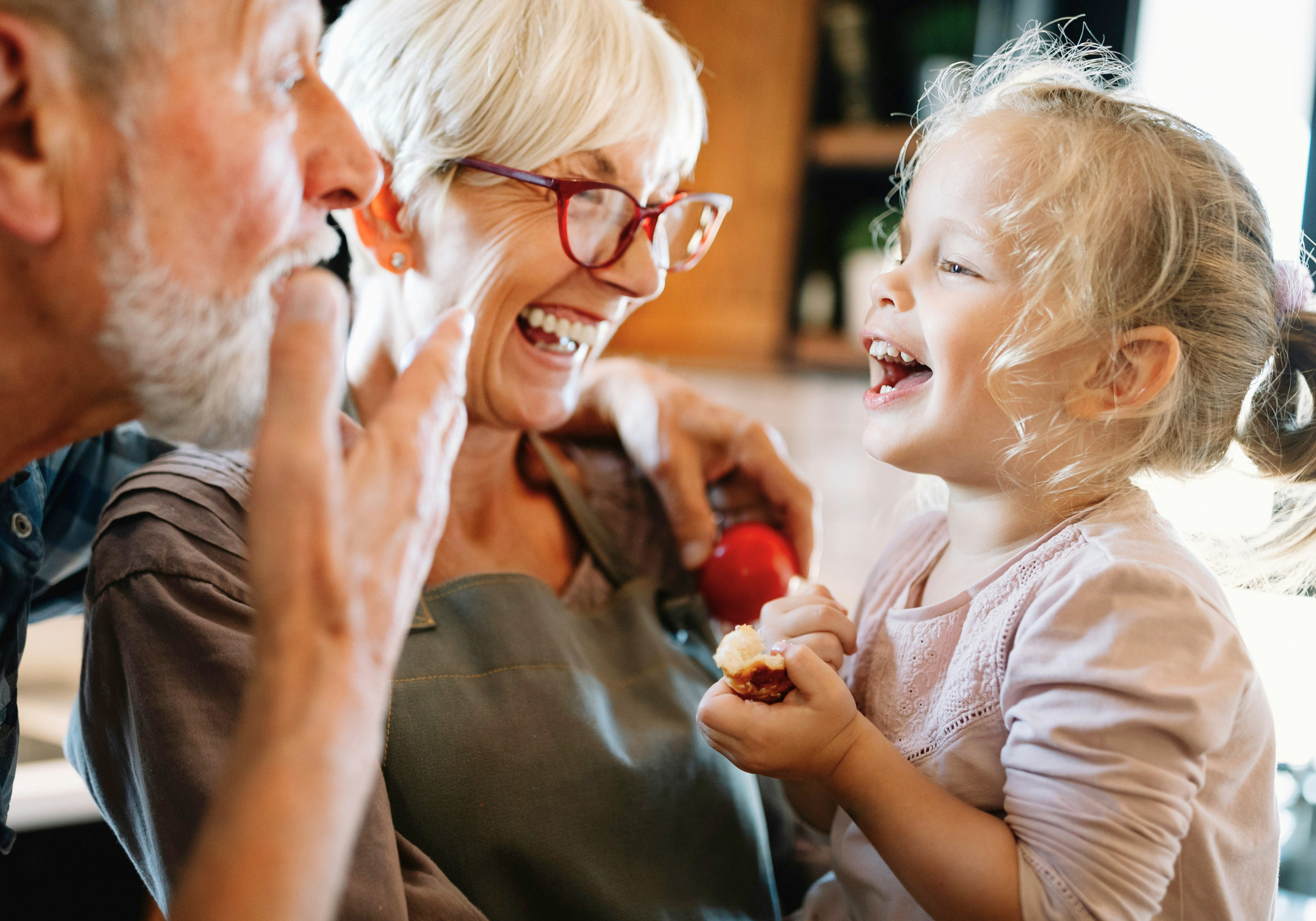 Grandmother holding her young grandaughter in her arms, with Grandfather beside her making them laugh