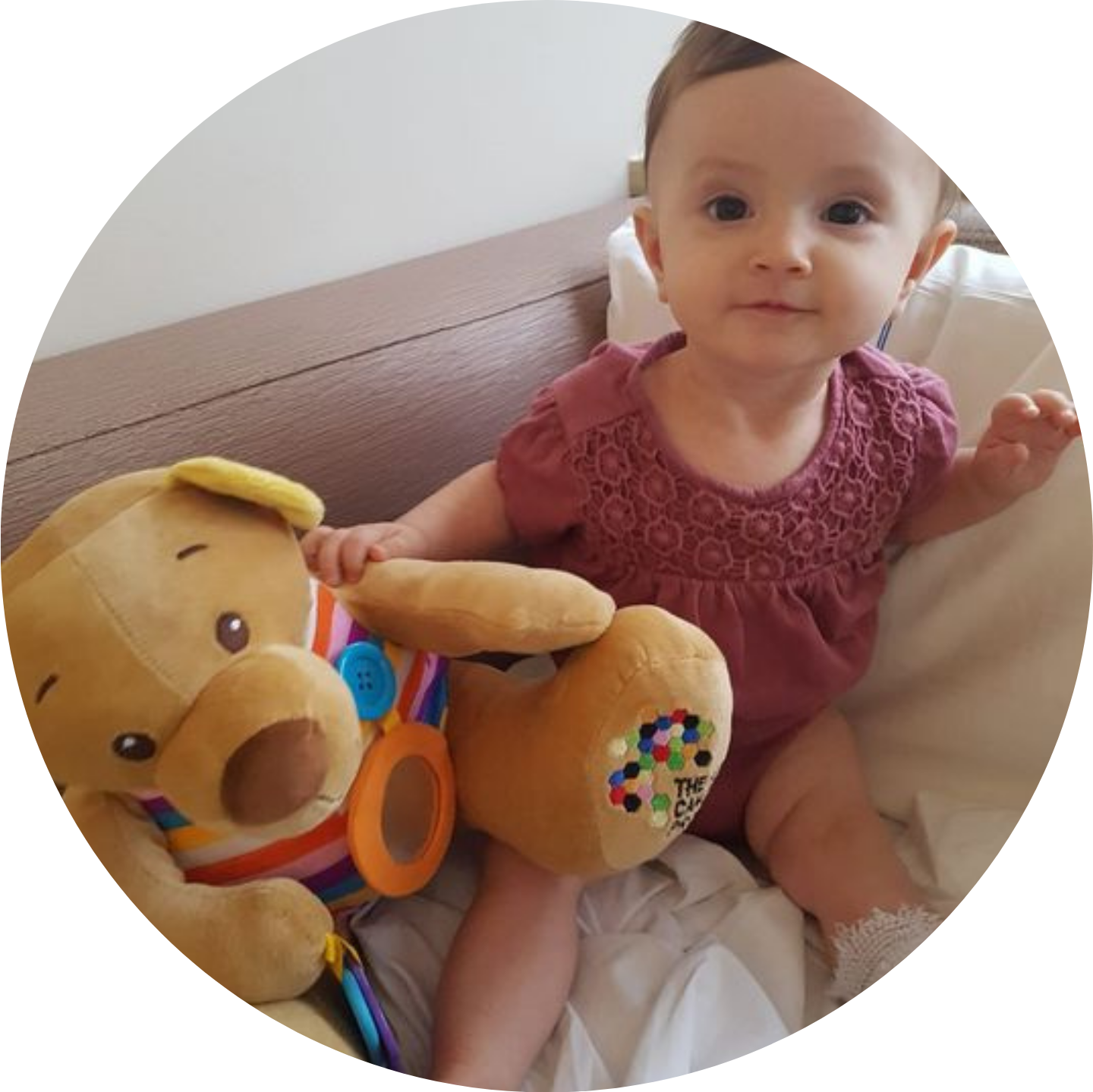 A small toddler plays with a TKCP bear that is dressed in a colourful, striped top.