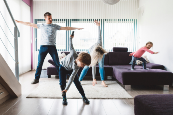 A family takes part in some stretching exercises together in a living room.