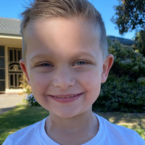 Ollie with his hair grown back, smiling out the front of his home