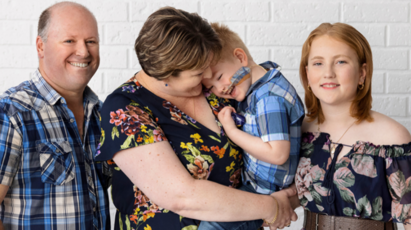 Jamie is held by his Mum and surrounded by his Dad and sister.