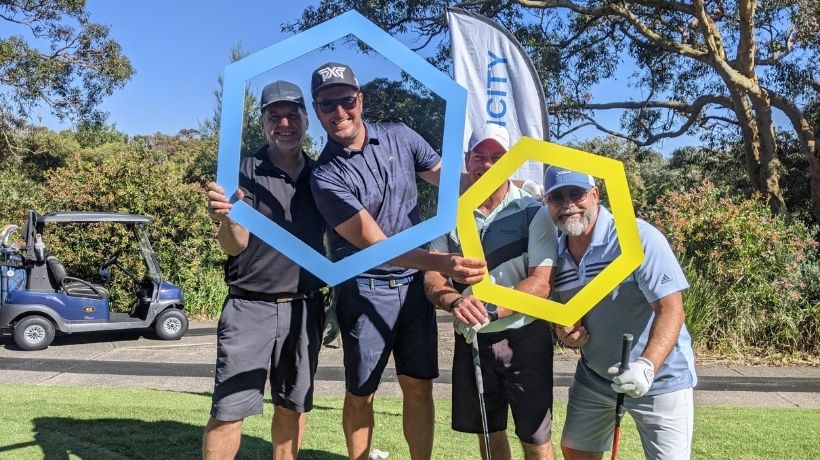 Eager golfers pose on the green with golf-clubs in hand and holding up brightly coloured hexagonal frames.