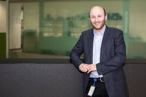 Associate Professor David Ziegler smiles while leaning against a handrail in the interior of a building.