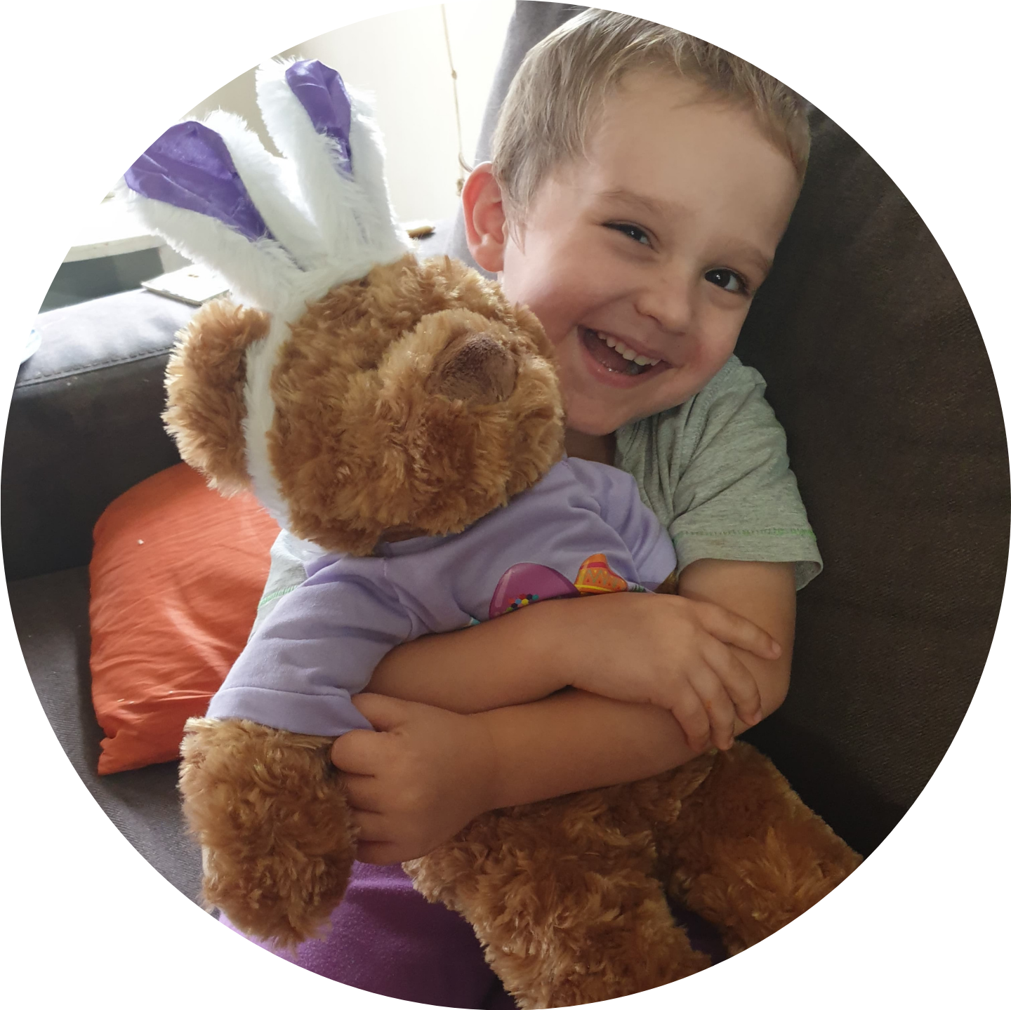 Parker smiles while hugging a TKCP bear dressed up in a purple t-shirt and bunny ears