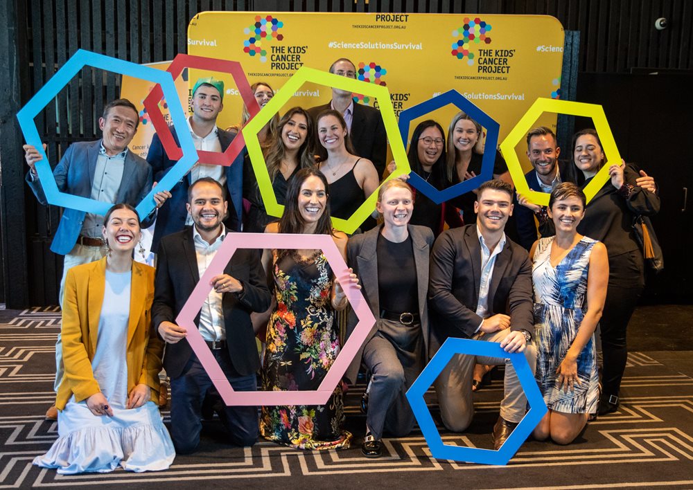 The WOTSO team at one of our events, standing in front of a yellow TKCP banner and holding up various hexagonally shaped frames