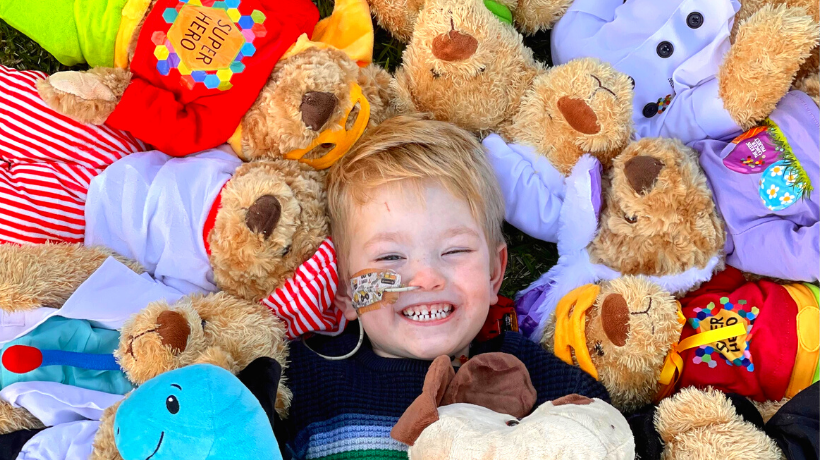 Jamie is lying on the ground, smiling with all his TKCP bears surrounding him.