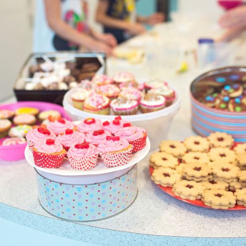 A display table is covered with brightly decorated and tasty treats including cupcakes and biscuits.