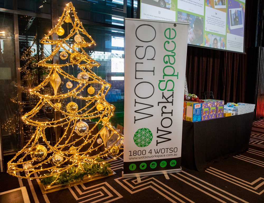 WOTSO's Christmas display consisting of a Christmas tree shaped frame, decorated with gold lights and ornaments and a banner for WOTSO WorkSpace on the right.