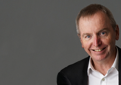 Associate Professor Geoff McCowage smiles at the camera against a neutral backdrop.