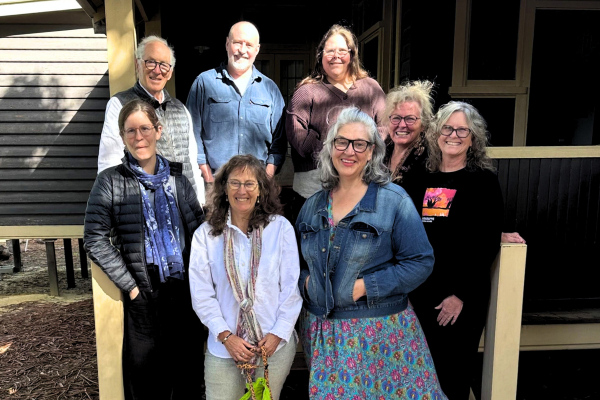 8 adults standing in a group on stairs infront of a house, all smiling at the camera.