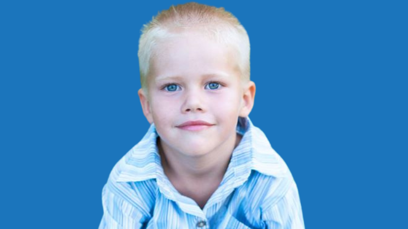 Zach is smiling at the camera wearing a pale blue shirt against a darker blue background.