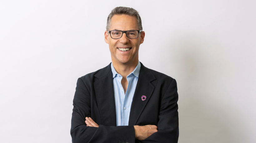 Professor Ricky Johnstone smiles with arms folded confidently in front of a white backdrop.