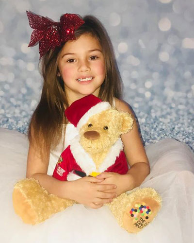 Girl with a big red bow in her hair hugging Santa bear
