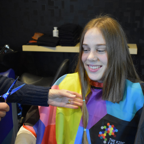 A student wears a TKCP smock and smiles as her very long hair is cut short for a fundraiser.