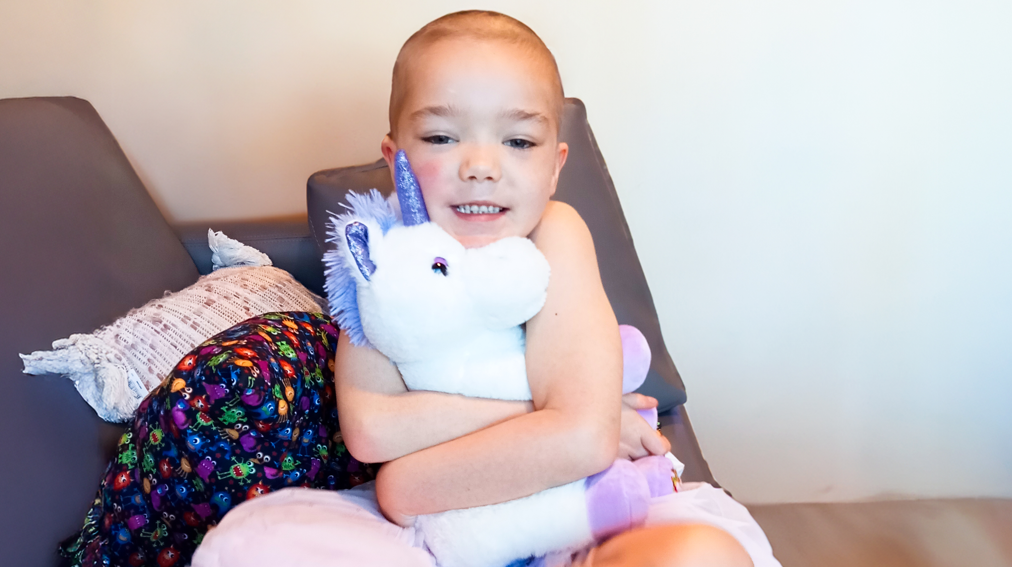 Maia is pictured cuddling with a variety of TKCP bears; she is smiling despite the challenges of her cancer treatment.