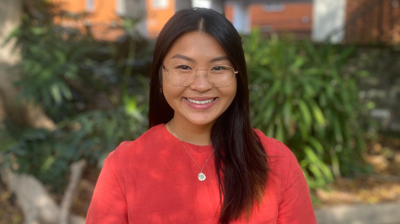 Lauren Ha is smiling at the camera with a green, leafy garden in the background.