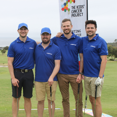 Four men in matching blue tee-shirts stand on the green with golf clubs in hand, in front of a TKCP banner.