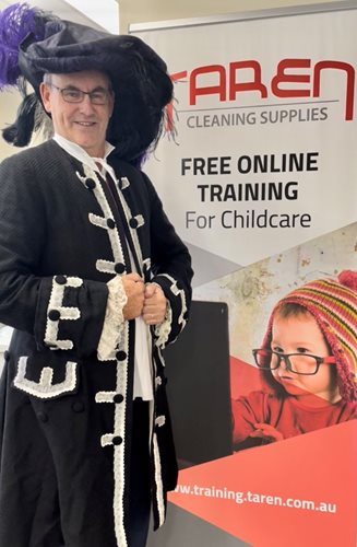 A man wears a full pirate costume, complete with feathered pirate hat, behind him is a banner advertising Taren Cleaning Supplies' free online training for childcare.