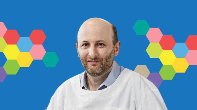 Associate Professor David Ziegler smiles with a blue backdrop decorated with colourful hexagonal shapes.