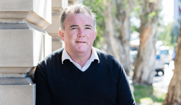 TKCP CEO Owen Finegan smiles while leaning against the facade of a building.