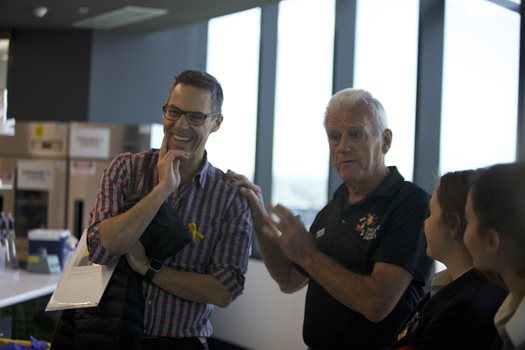 Col Reynolds and Professor Ricky Johnstone have a lively conversation with a group of people.