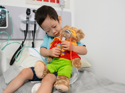 A small child cuddles a teddy bear that has an oxygen mask on, demonstrating the treatment that will be provided.